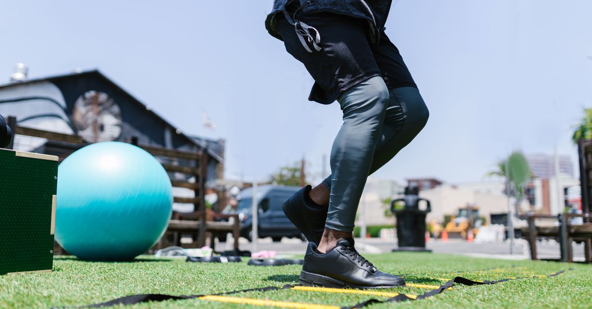 Person exercising outdoors with fitness gear and agility ladder on grass.